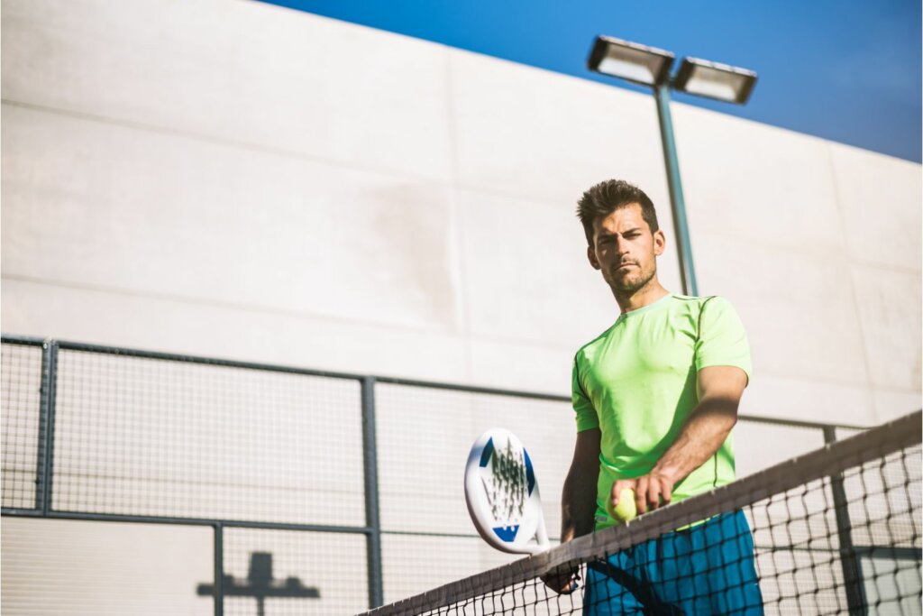 homme portant t-shirt vert fluo et short bleu près du filet du court de Padel