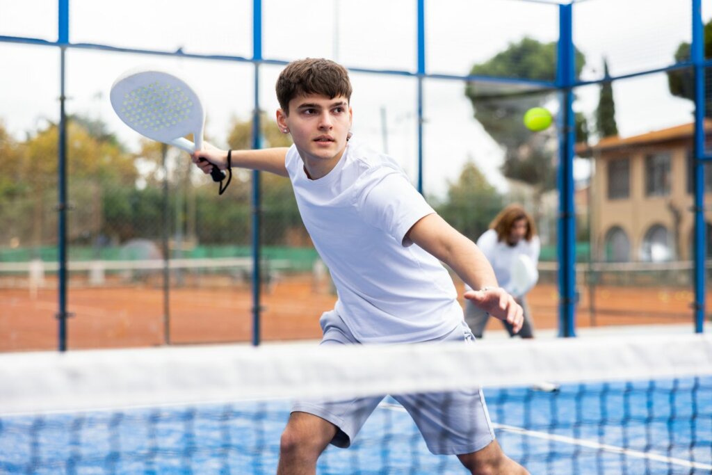 jeune joueur de Padel, portant une tenue blanche e raquette à la main sur le court