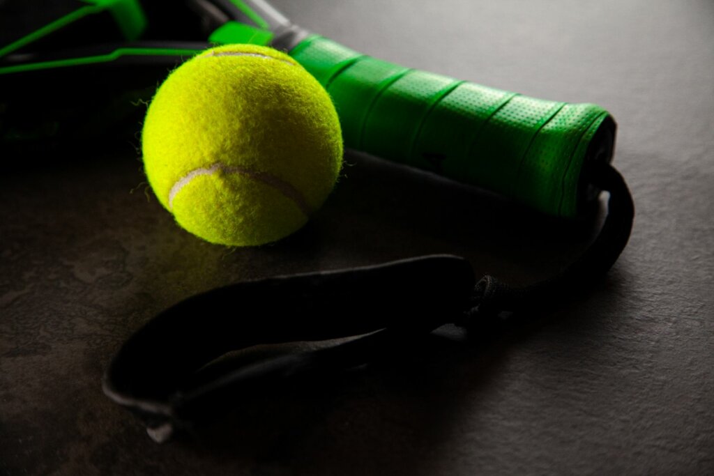 une balle jaune de Padel près d'une raquette noire avec manche et grip en vert
