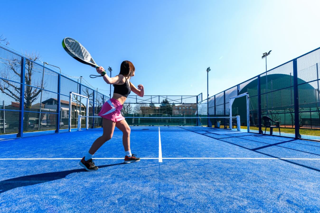 court de Padel en bleu et une joueuse tient une raquette noire et blanche dans sa main, prête à frapper