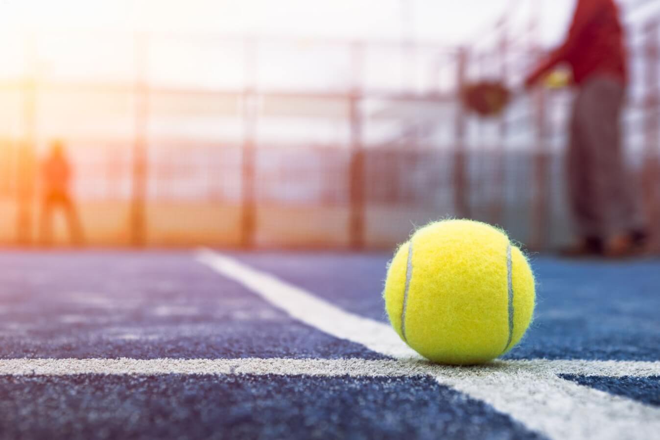 balle de Padel jaune sur le sol d'un terrain et en arrière plan, 2 joueurs de Padel