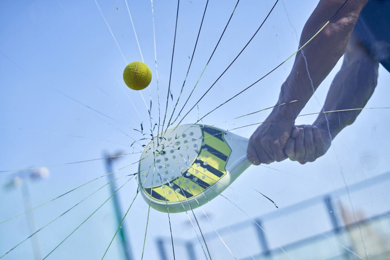un mur en verre qui se casse après un coup violent d'une raquette blanche avec un peu de jaune et noir et une balle