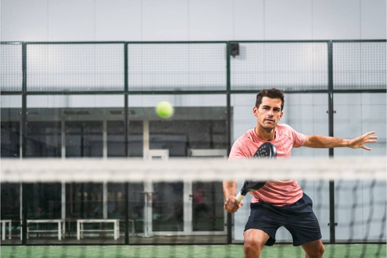 un homme jouant au Padel en tenue de sport prêt à frapper la balle jaune avec sa raquette de Padel noire