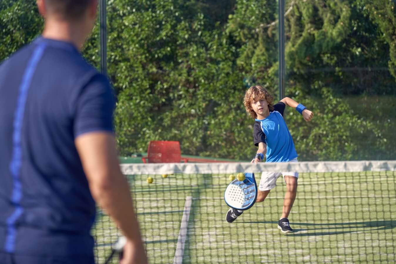 un enfant portant un t-shirt bleu et short blanc tenant une raquette à la main sur un terrain