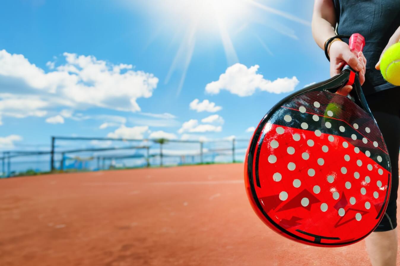 une raquette noire et rouge tenue par de petites mains sous le soleil