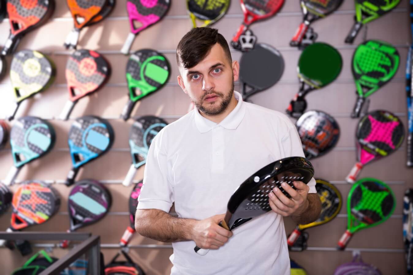 un joueur portant un polo blanc tenant à la main une raquette neuve dans une boutique