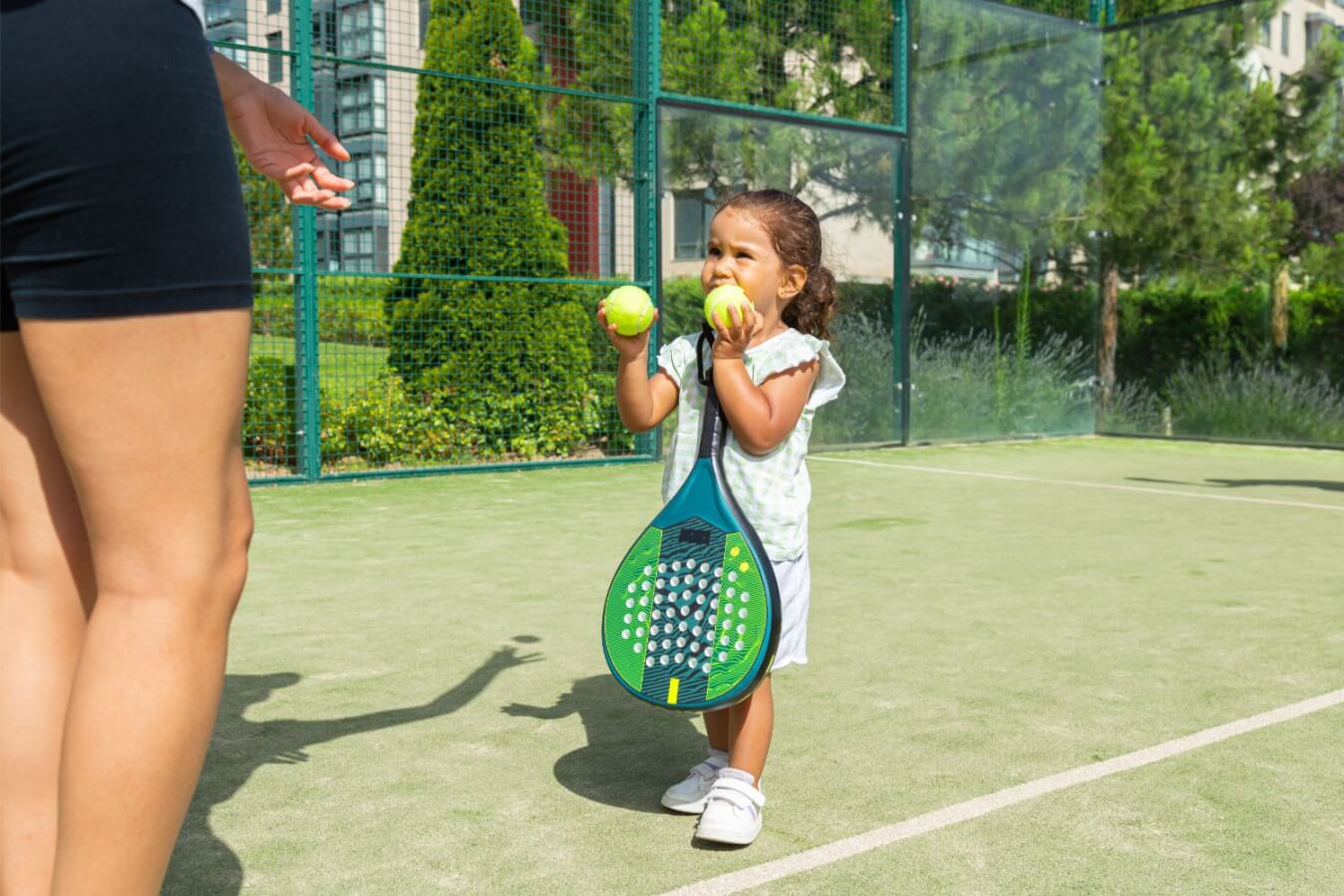 petite fille tenant 2 balles jaunes et une raquette sur un terrain de Padel en gazon