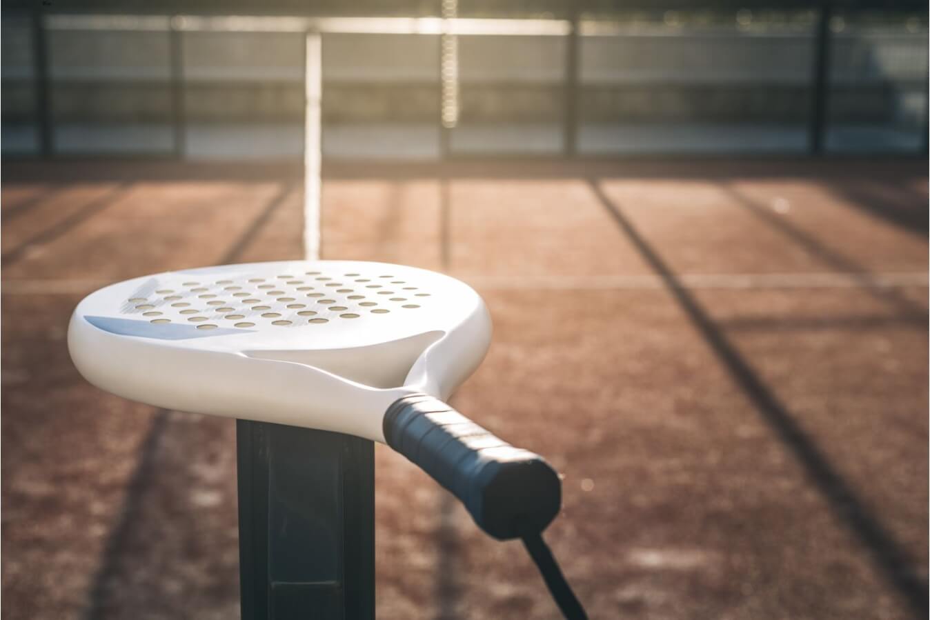 une raquette de Padel placée sur le poto du filet d'un terrain