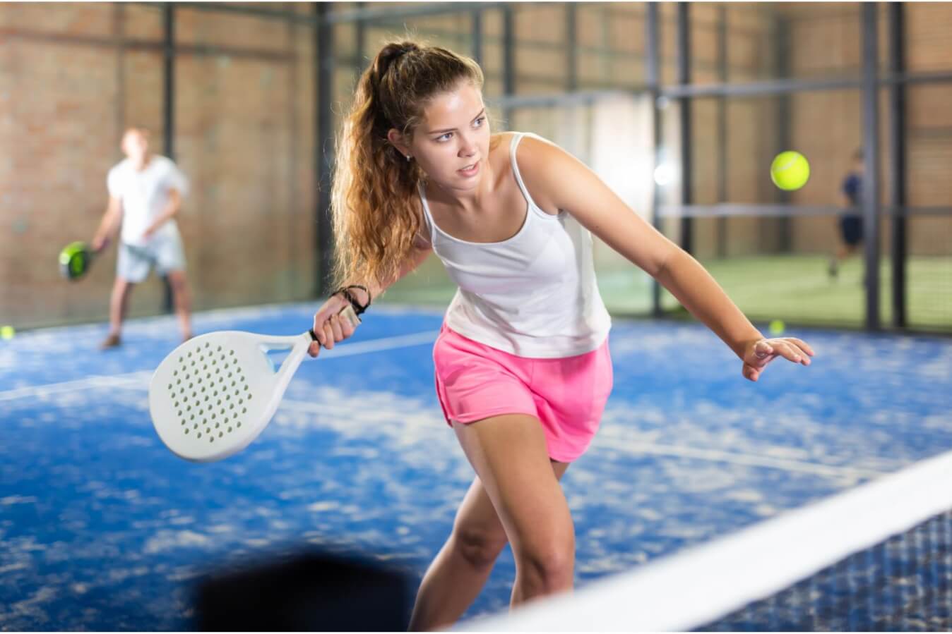 une joueuse portant un short rose et un débardeur blanc, raquette à la main prête à frapper la balle