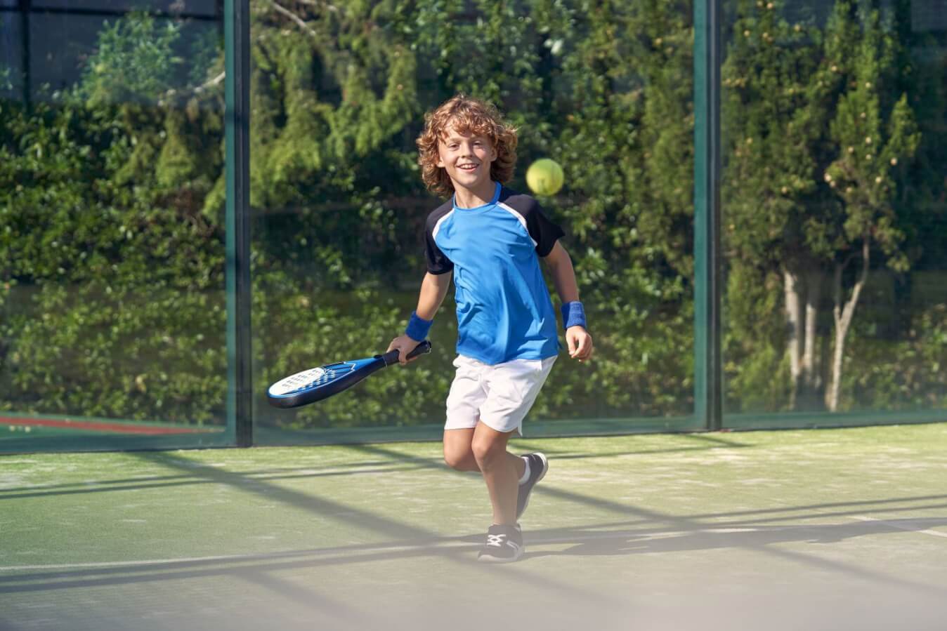 un enfant avec tenue bleu et blanc tenant une raquette à la main sur le terrain de Padel