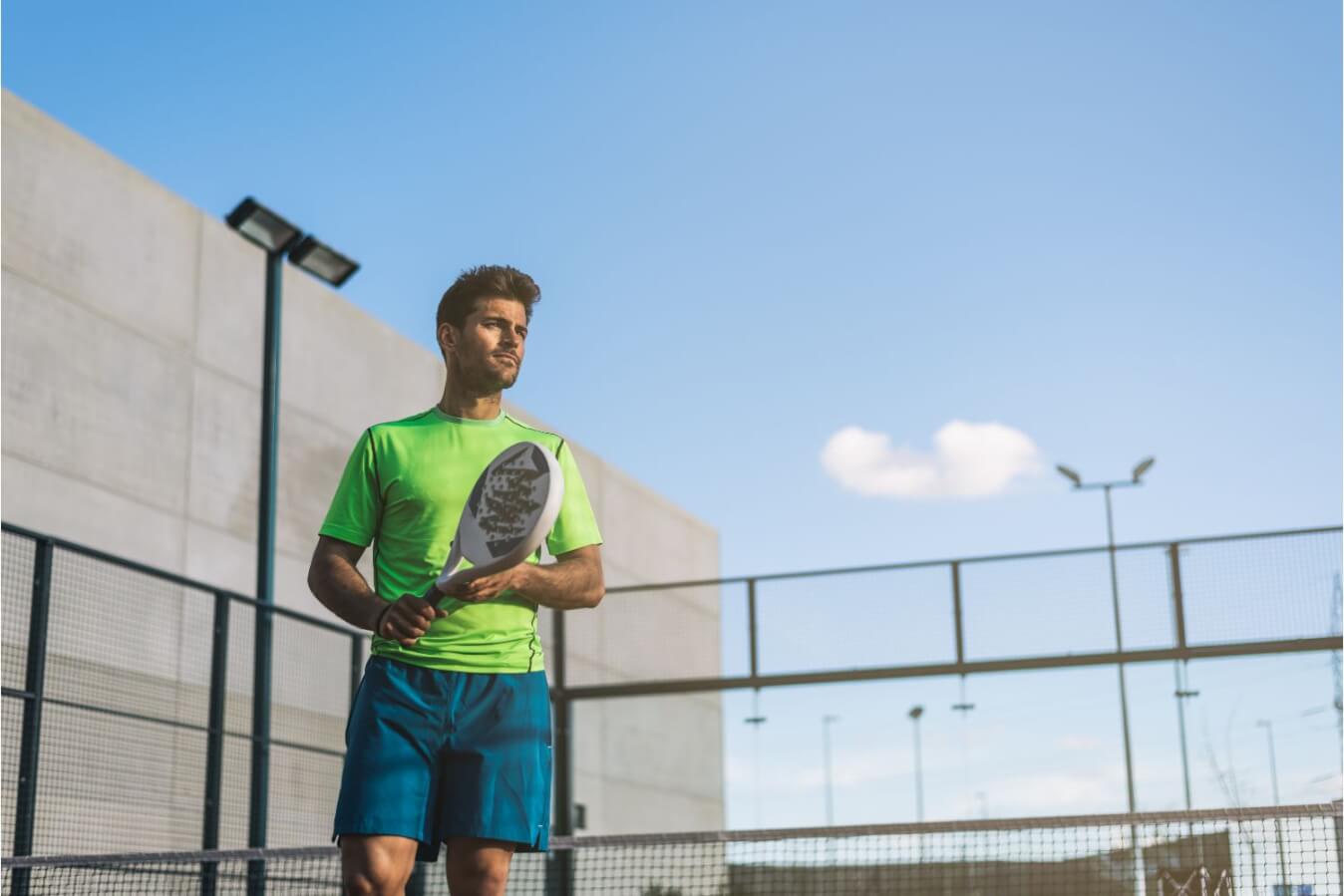 joueur de Padel en tenue verte et bleue avec raquette à la main sur un terrain