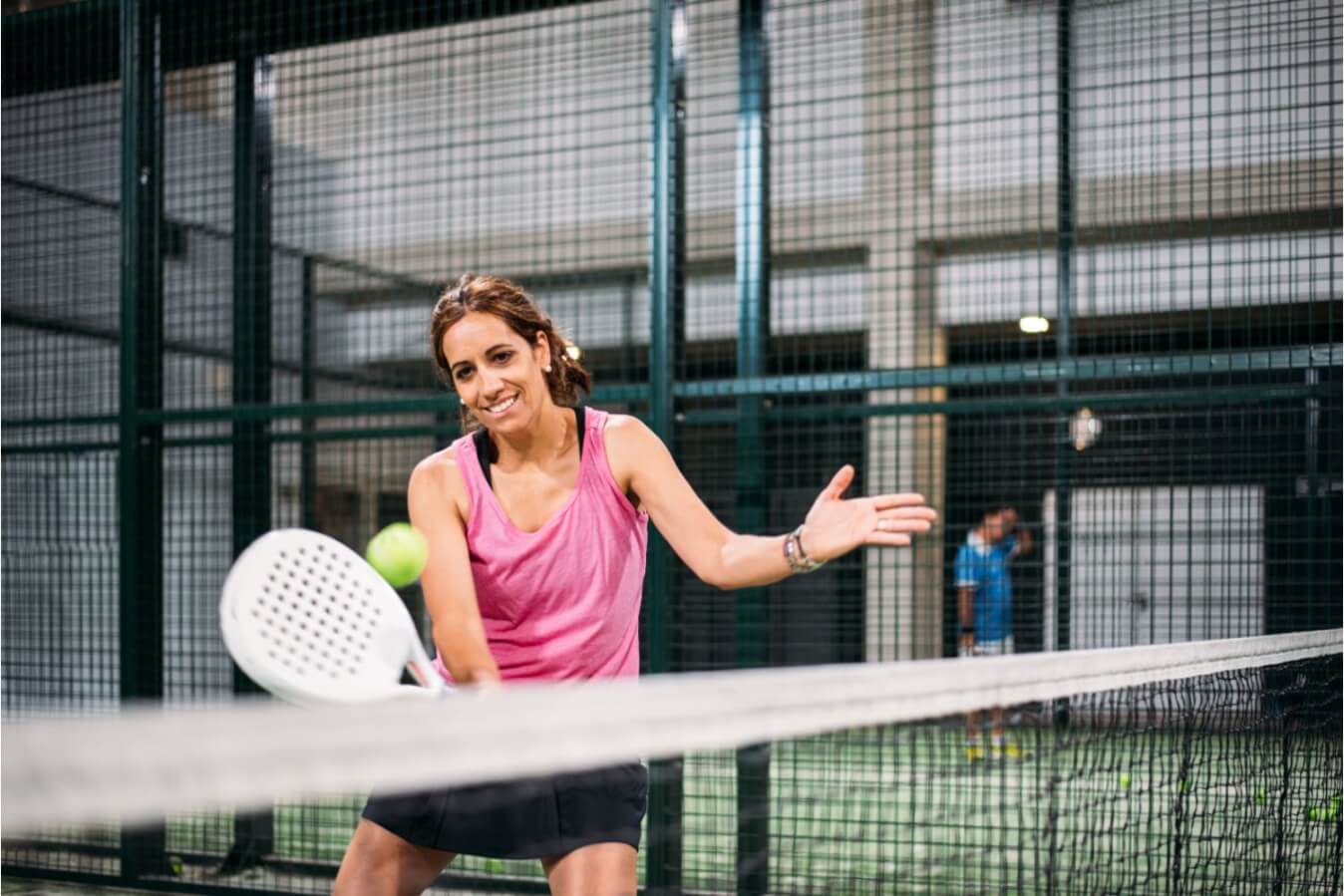 une joueuse de Padel portant un t-shirt rose et short noir avec raquette à la main prête à frapper une balle près du filet