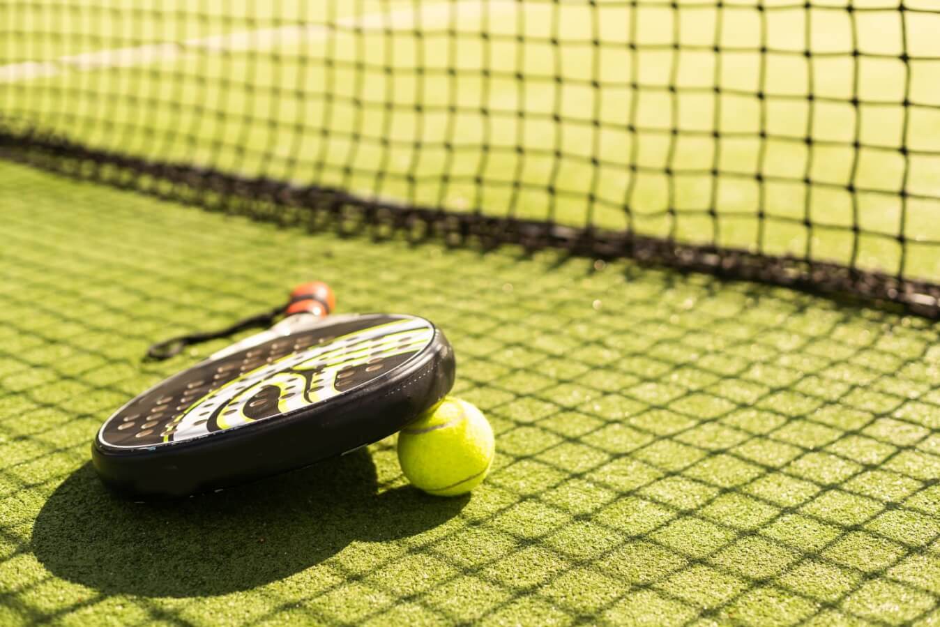 raquette de Padel noire et blanc sur une balle jaune, le tout sur un terrain en gazon près du filet