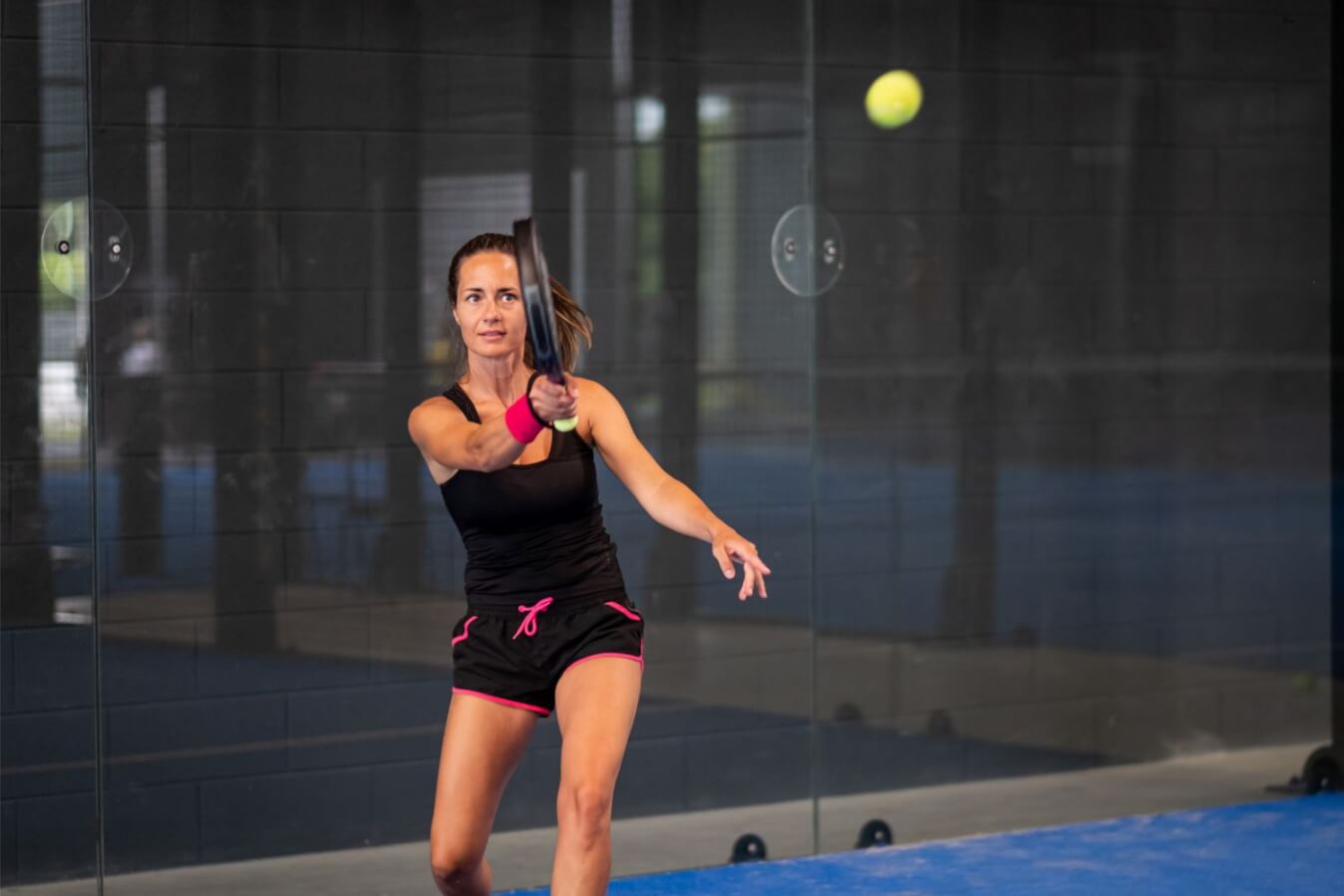 joueuse de Padel en tenues noire et rose avec raquette à la main, prête à frapper la balle