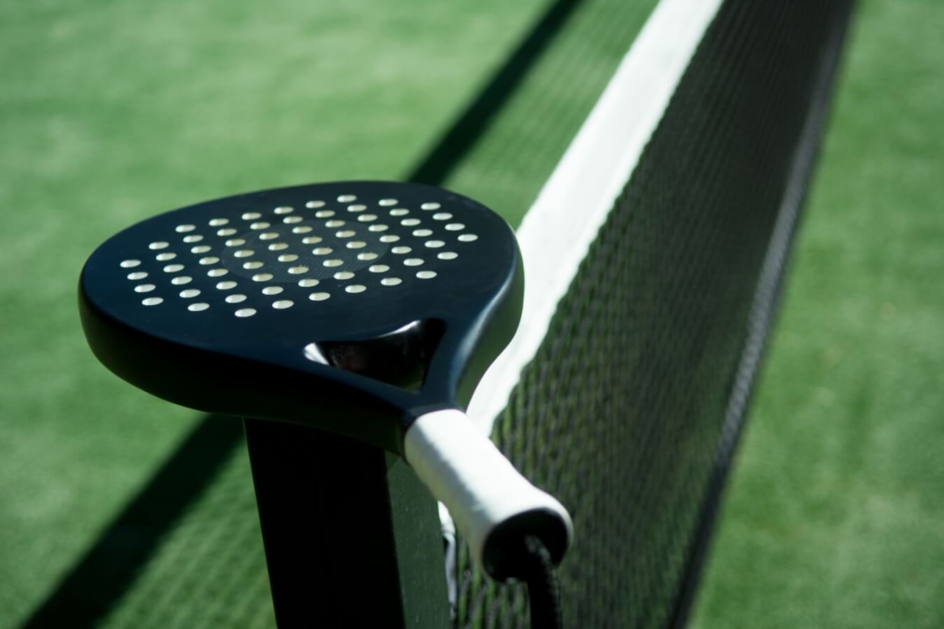 raquette de Padel posée sur le poto du filet d'un terrain de Padel