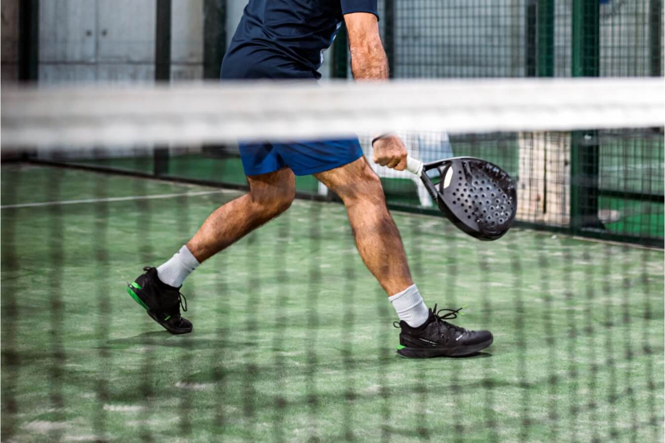 joueur de Padel près du filet portant des chaussures noires et vertes, raquette à la main