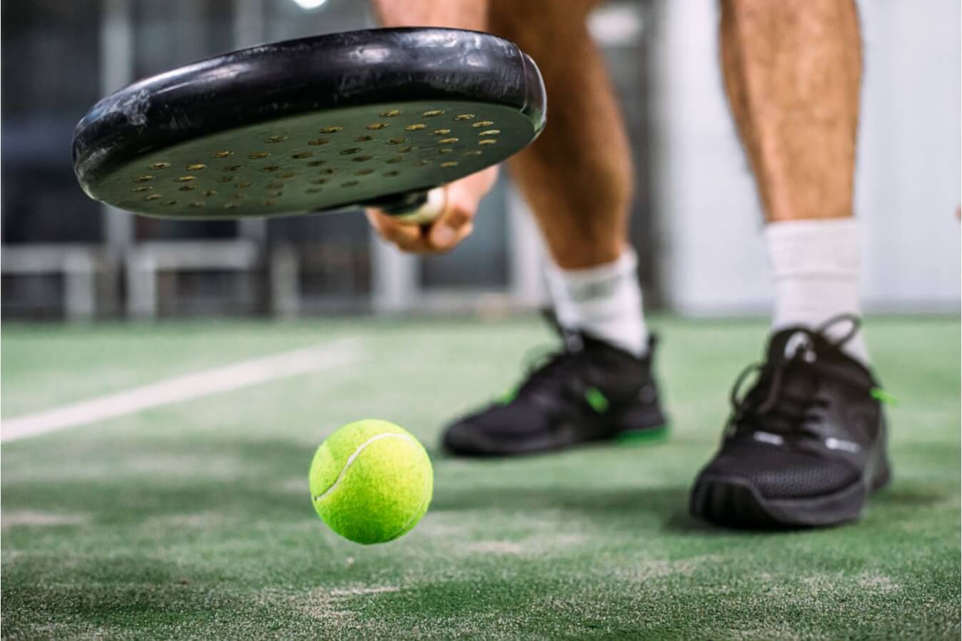 chaussures de Padel noires, raquette et balle jaune sur le terrain en gazon