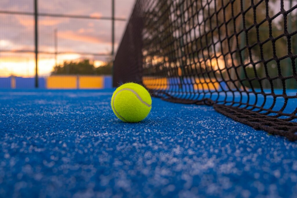 Balle de Padel jaune placée sur le sol bleu d'un terrain de Padel près du filet