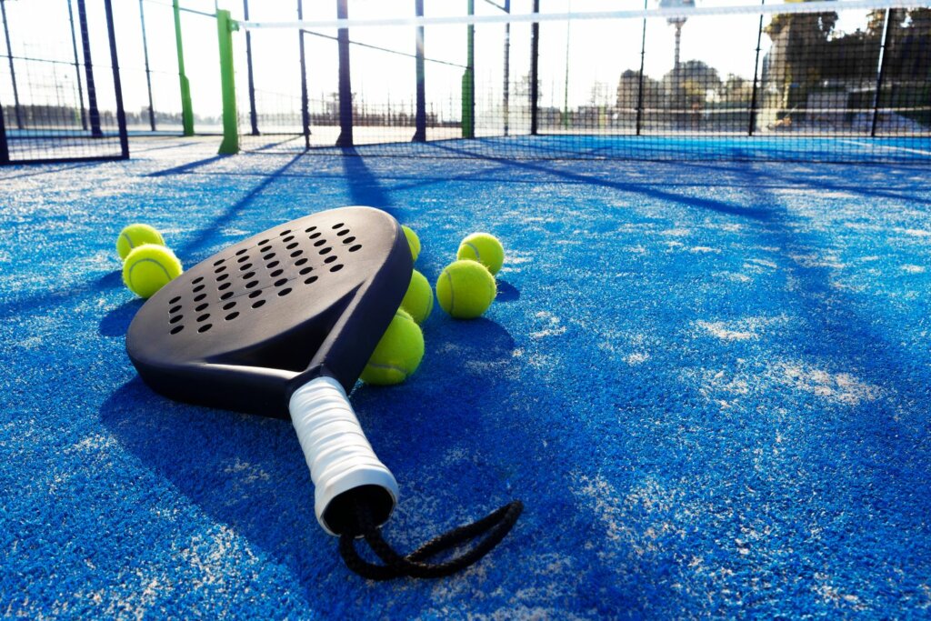 des balles jaunes de Padel et une raquette noire avec grip blanc placés sur le sol en bleu du terrain