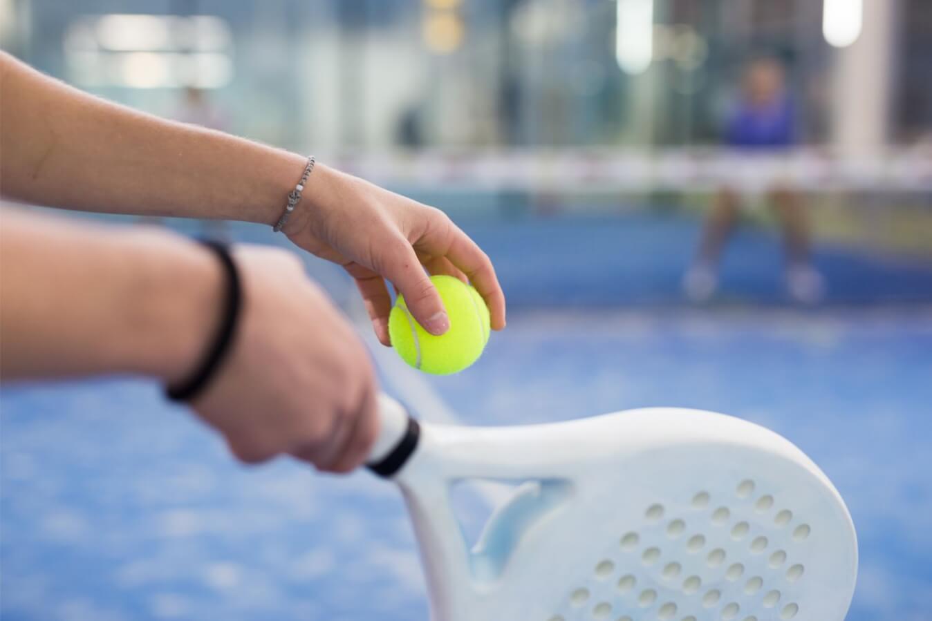 une main tenant une balle et une raquette de Padel