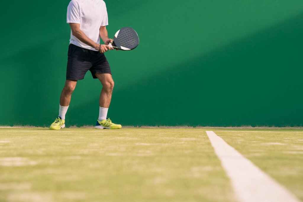 joueur e Padel avec chaussures jaune et raquette au fond du court