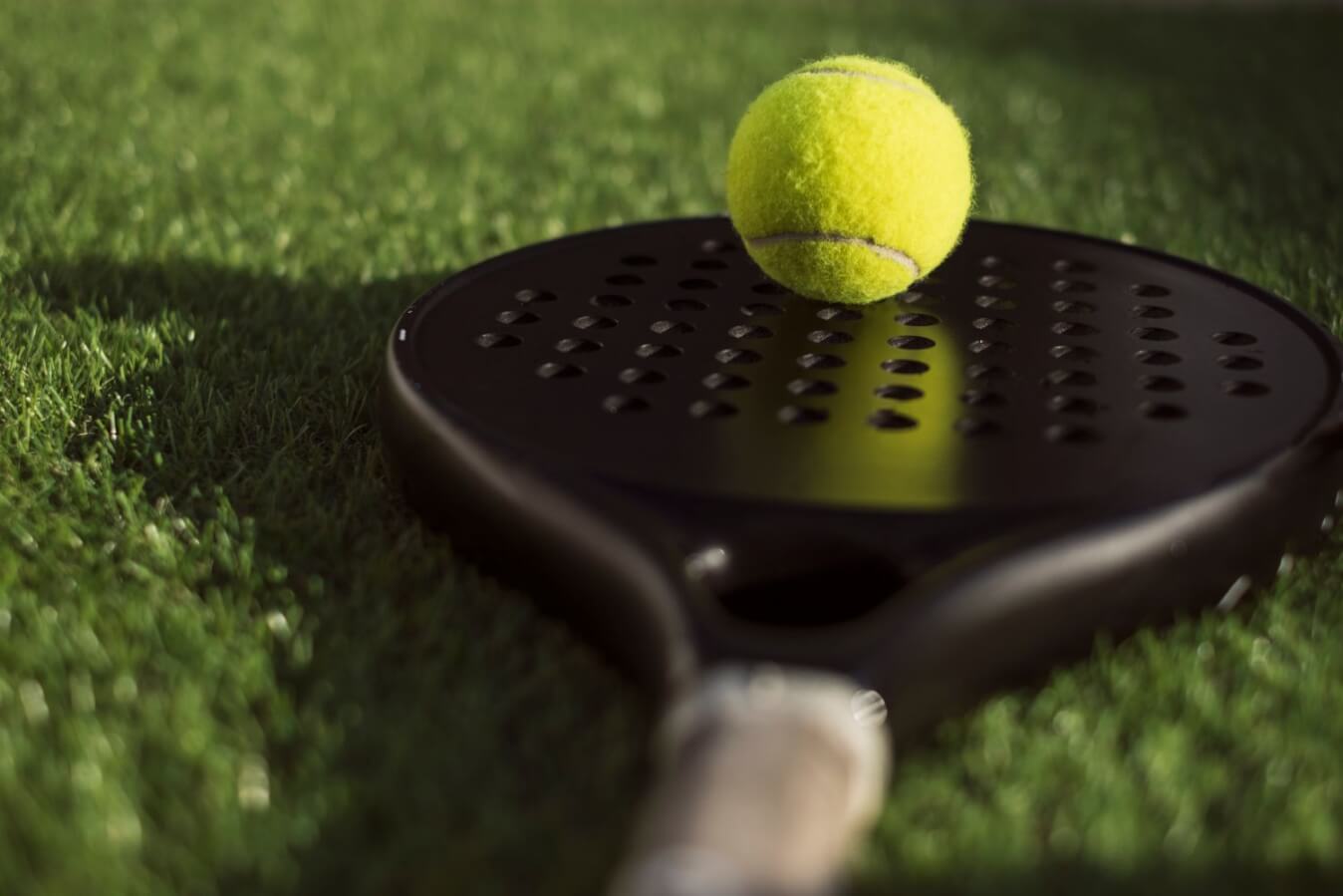 raquette de Padel noire posée sur un sol en gazon et dessus, une balle jaune
