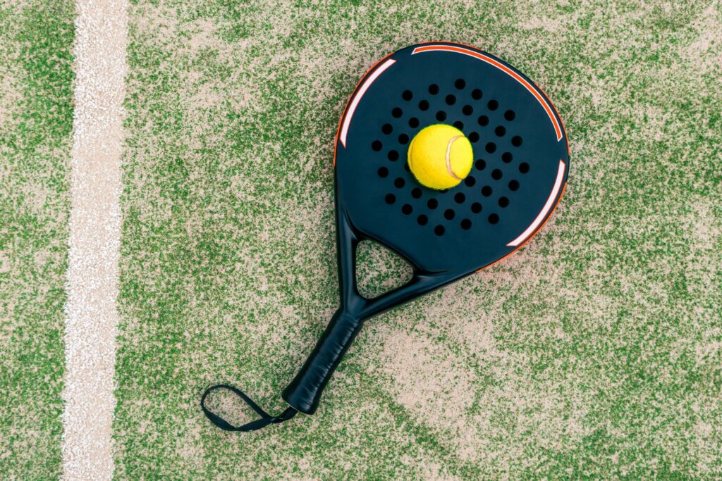raquette noire posée sur le gazon et sur le dessus au centre, une balle de Padel