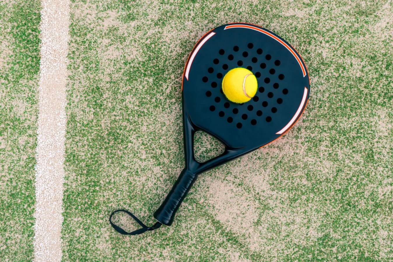 raquette noire posée sur le gazon et sur le dessus au centre, une balle de Padel