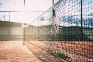 filet de Padel où est accroché une raquette et des balles jaunes par terre