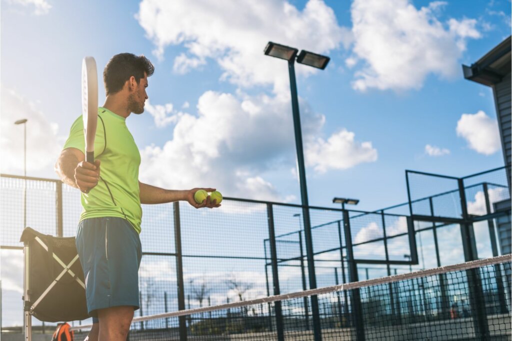 joueur de Padel tenant une raquette et des balles sur le terrain
