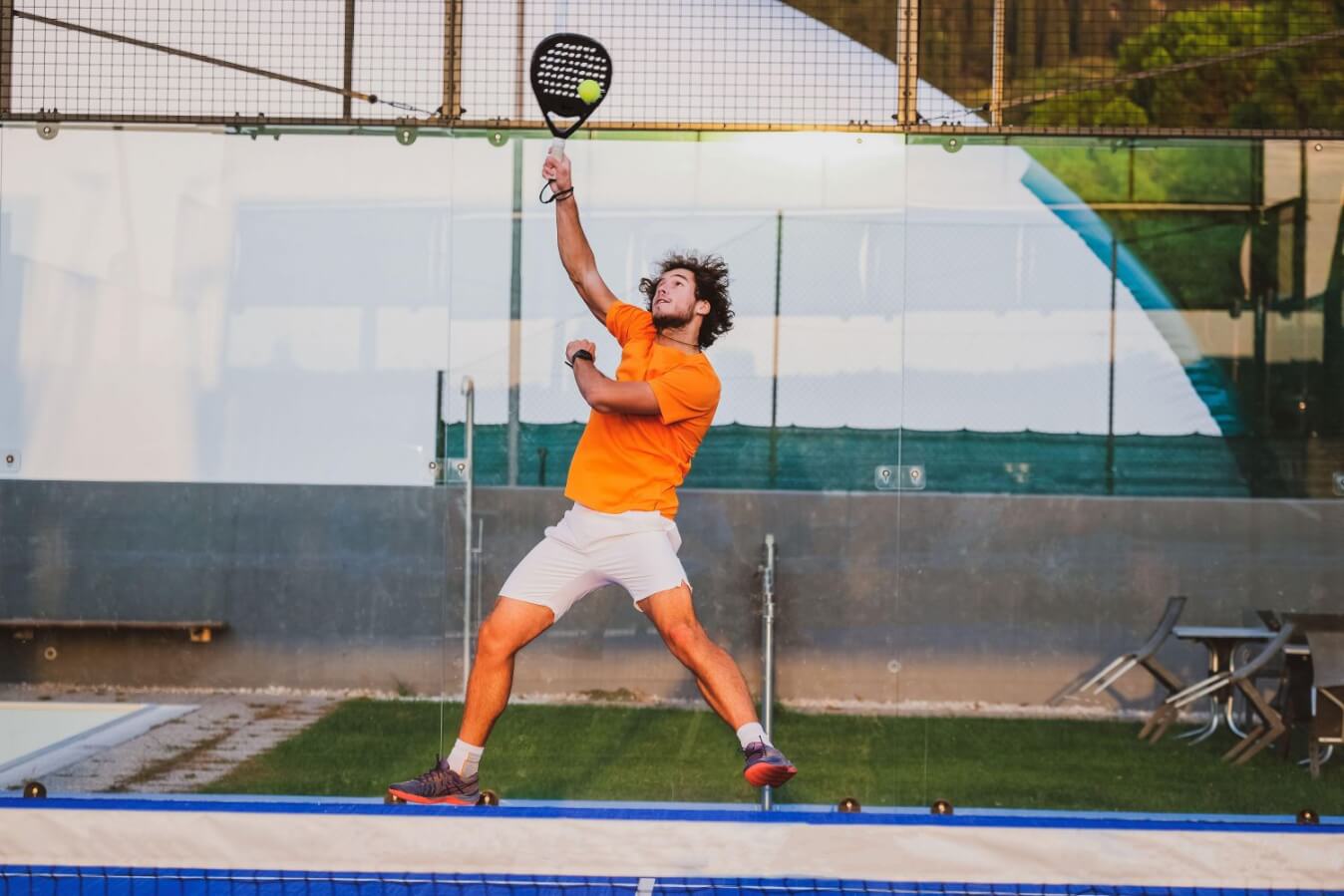 un joueur levant haut sa raquette de Padel sur le terrain pour frapper une balle