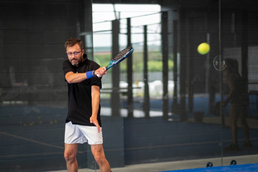 joueur de Padel en t-shirt noir et short blanc avec lunettes et raquette de Padel à la main