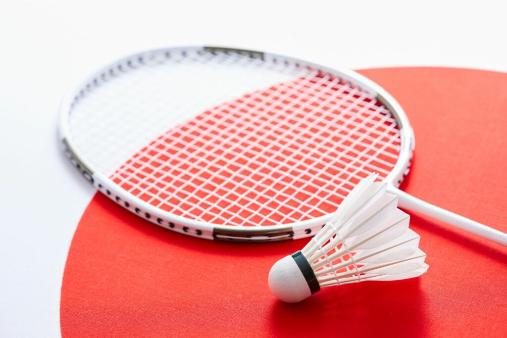 raquette de badminton blanche avec un peu de noire près d'un volant de la même couleur sur une table rouge