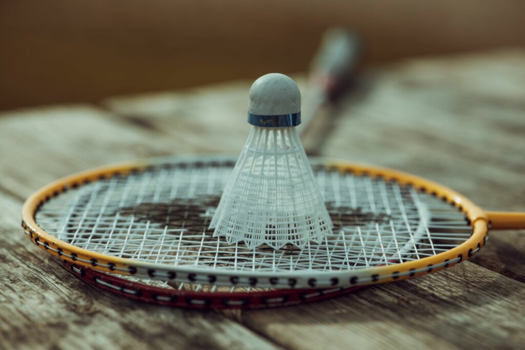 2 raquettes de badminton rouge et jaune et un volant sur le dessus, le tout sur un support en bois