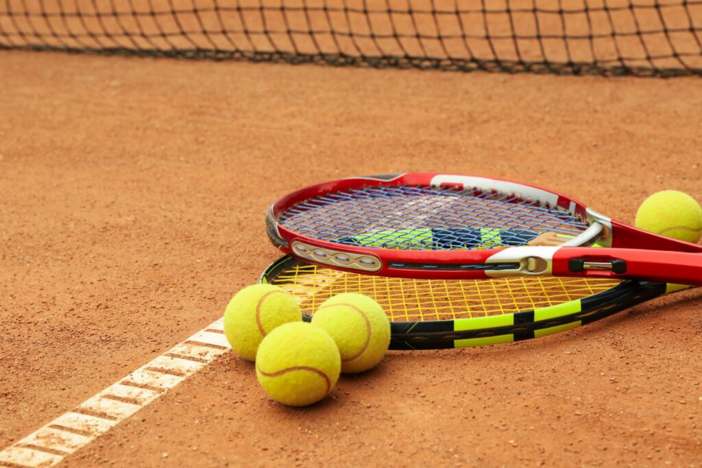 2 raquettes de tennis et 4 balles jaunes posées sur un sol en sable près du filet