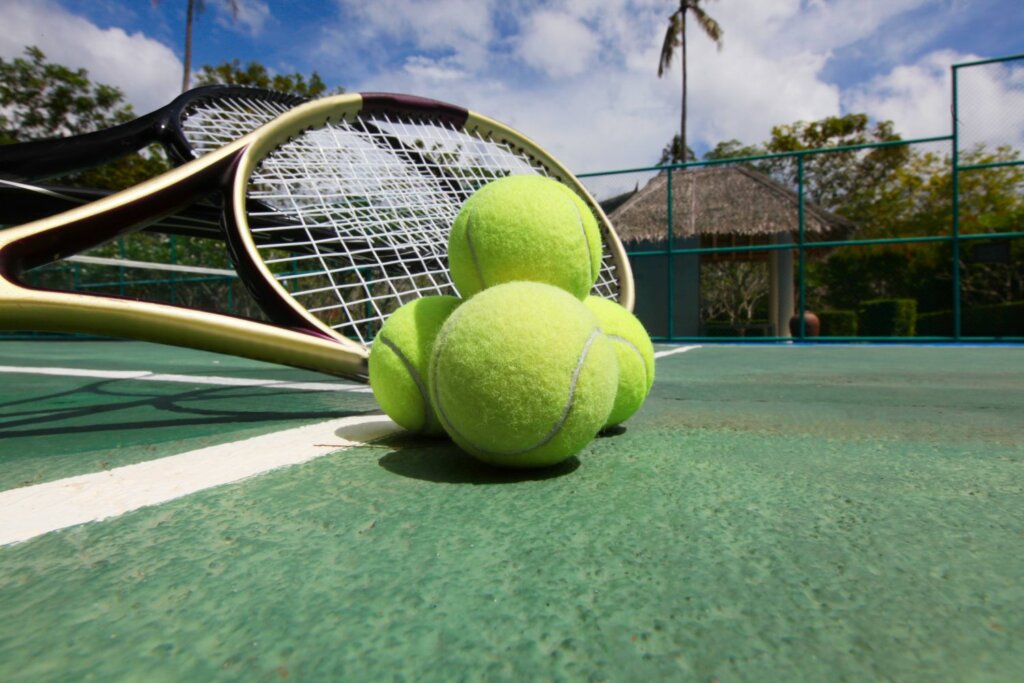 2 raquettes de tennis de couleur noire et jaune près de 3 balles jaunes, le tout posé sur un sol de couleur vert