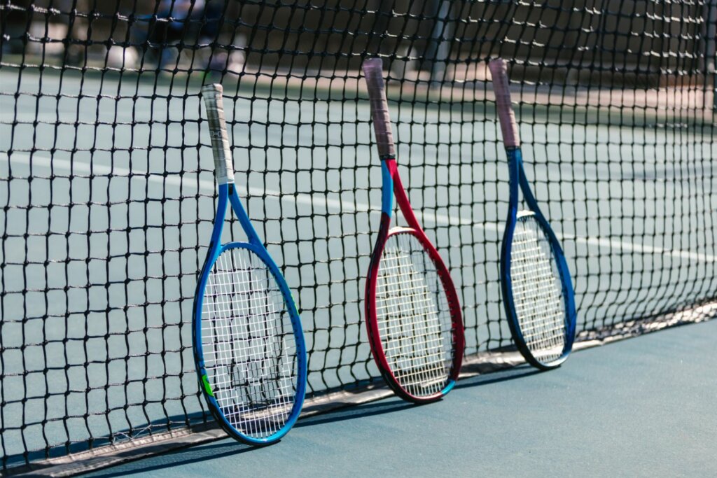 3 raquettes de tennis adossées contre le filet d'un terrain