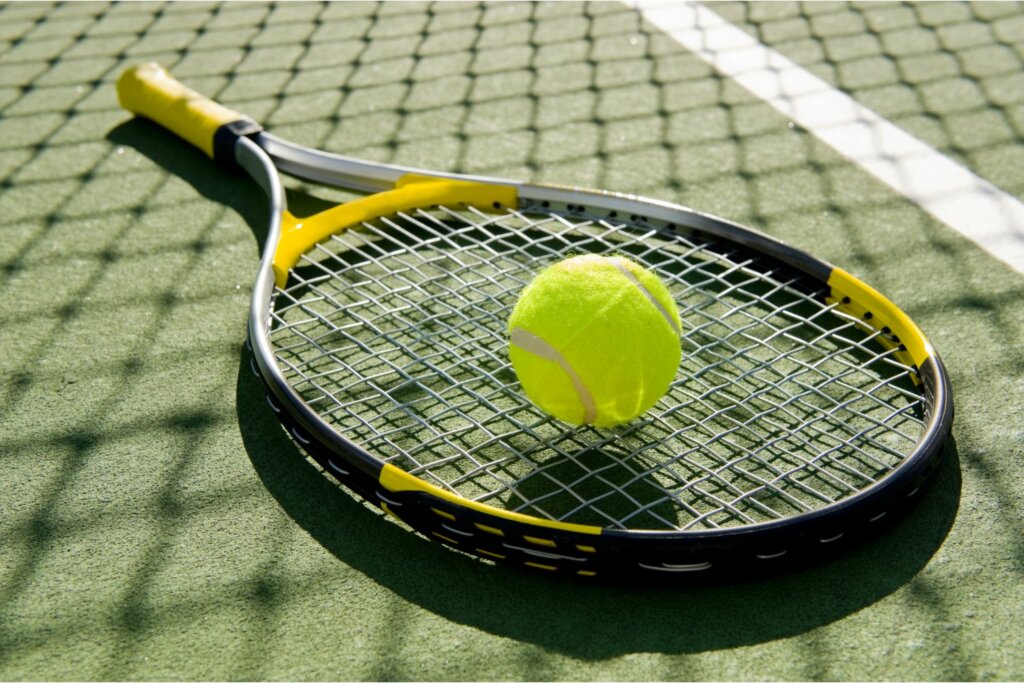 raquette de tennis noir et jaune posée sur le sol en gazon et une balle jaune sur les cordes de la raquette