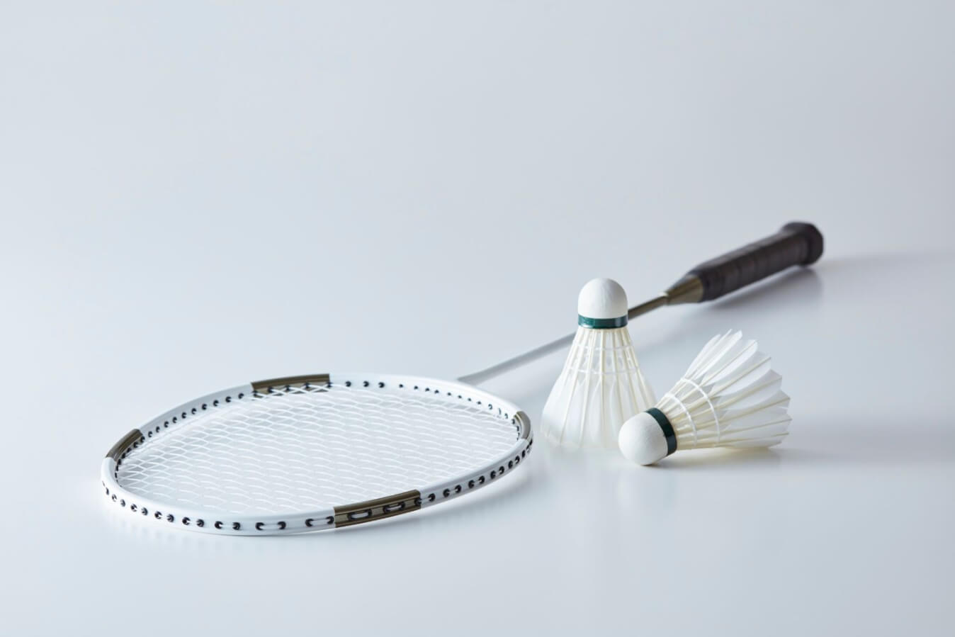 2 volants et une raquette de badminton posés sur un sol tout blanc