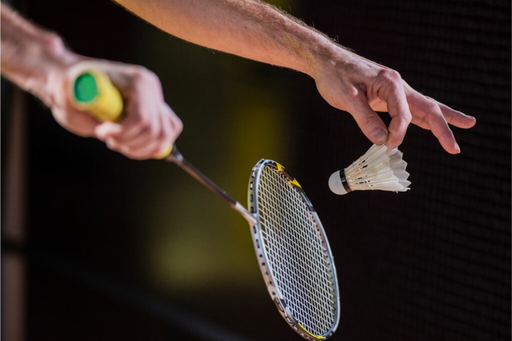 2 mains d'un joueur de badminton tenant une raquette et un volant sur un fond noir