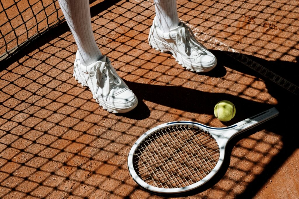 tennis blanc près du filet et de la raquette ainsi qu'une balle jaune de tennis