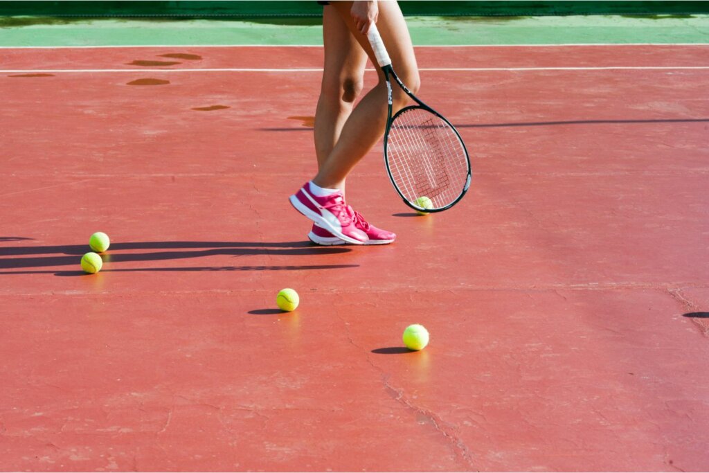 terrain de tennis, pied avec chaussure de tennis et des balles sur le sol ainsi qu'une raquette