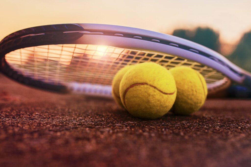 3 balles de tennis sous une raquette en plein coucher de soleil