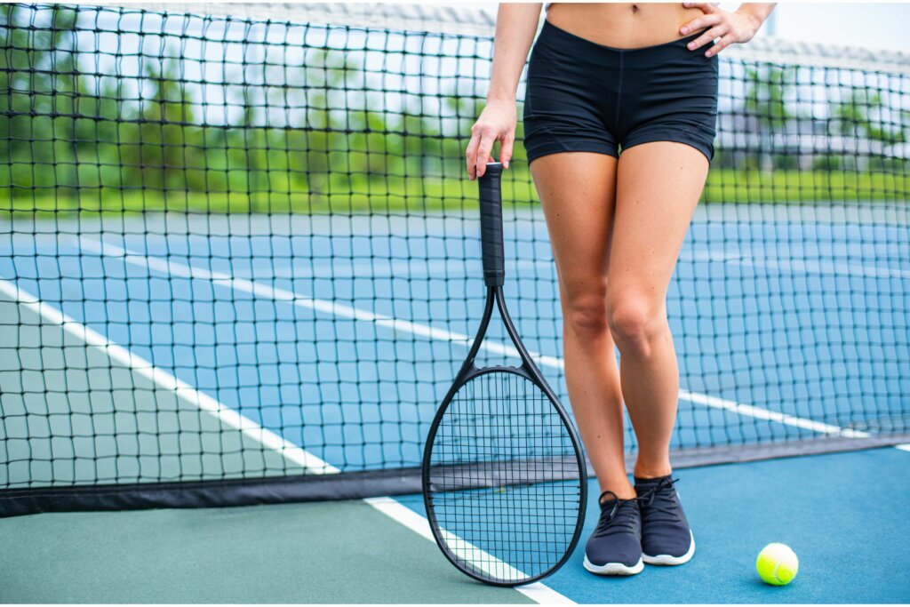 jambe d'une joueuse de tennis portant short noir et une chaussure noire, raquette et balle près du filet