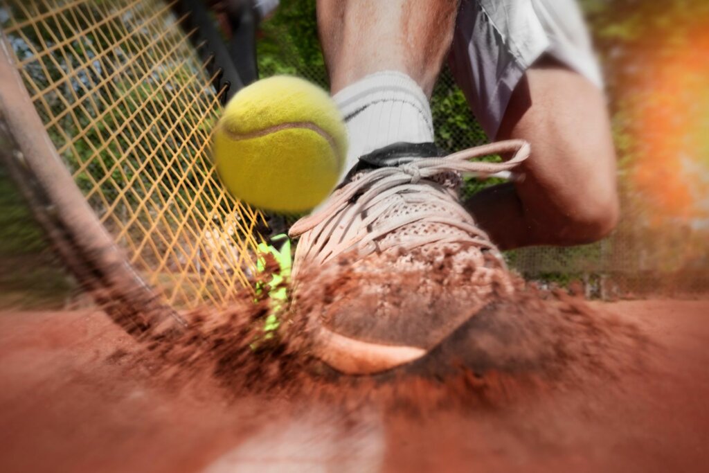 raquette de tennis et balle jaune ainsi qu'une chaussure glissant sur le sol en sable