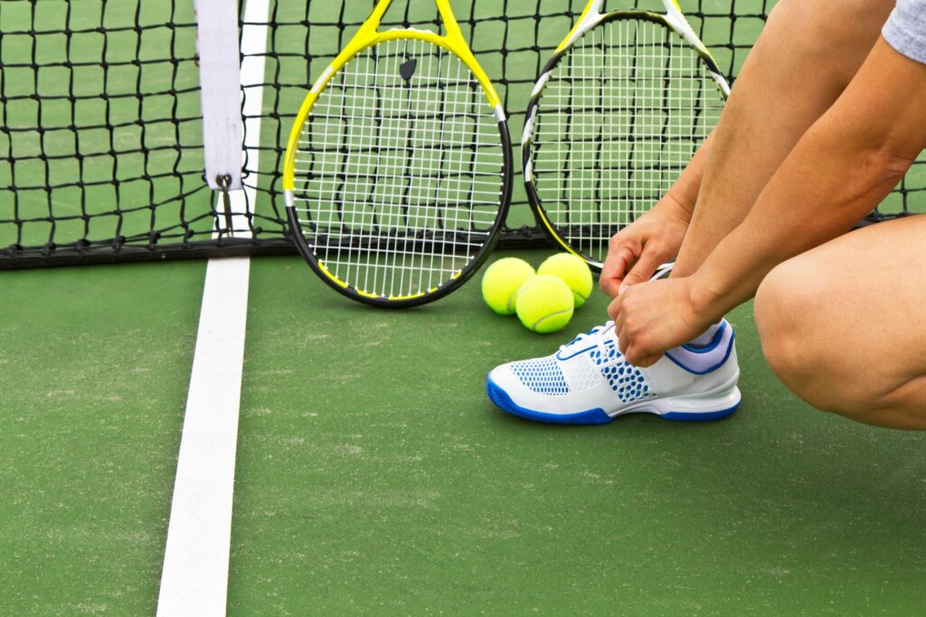 raquette de tennis et balles jaunes adossées sur le filet et près d'une chaussure blanche