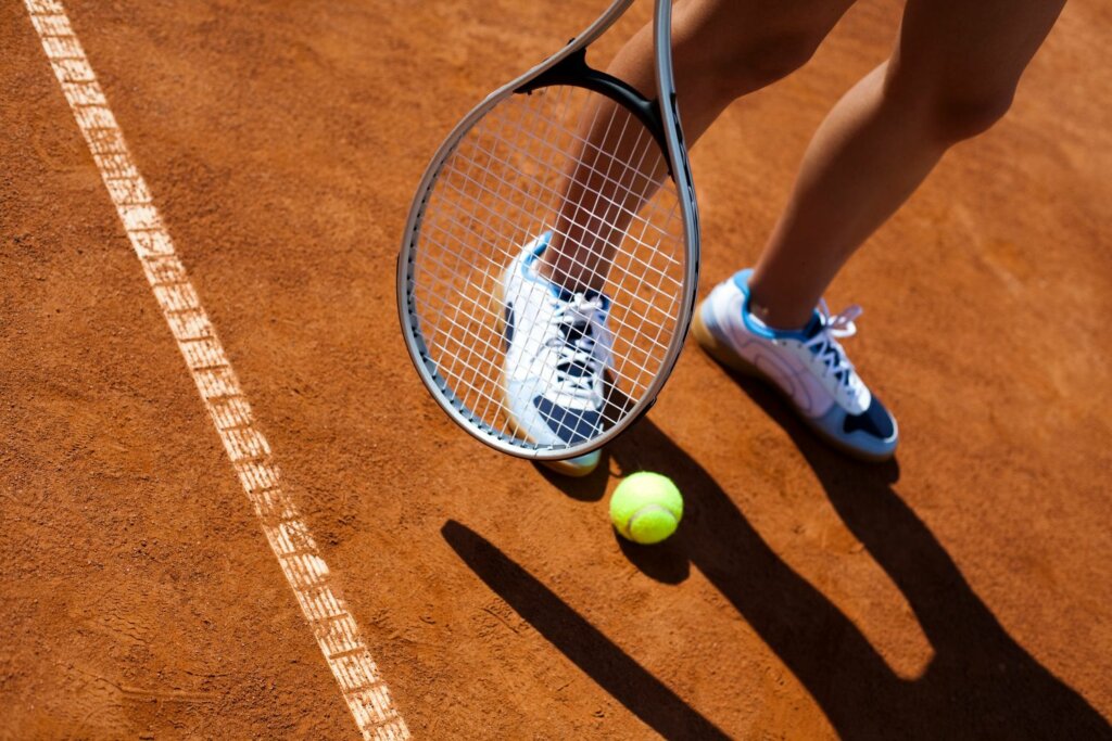pied avec chaussures blanches, raquette et balle de tennis sur le sol en sable