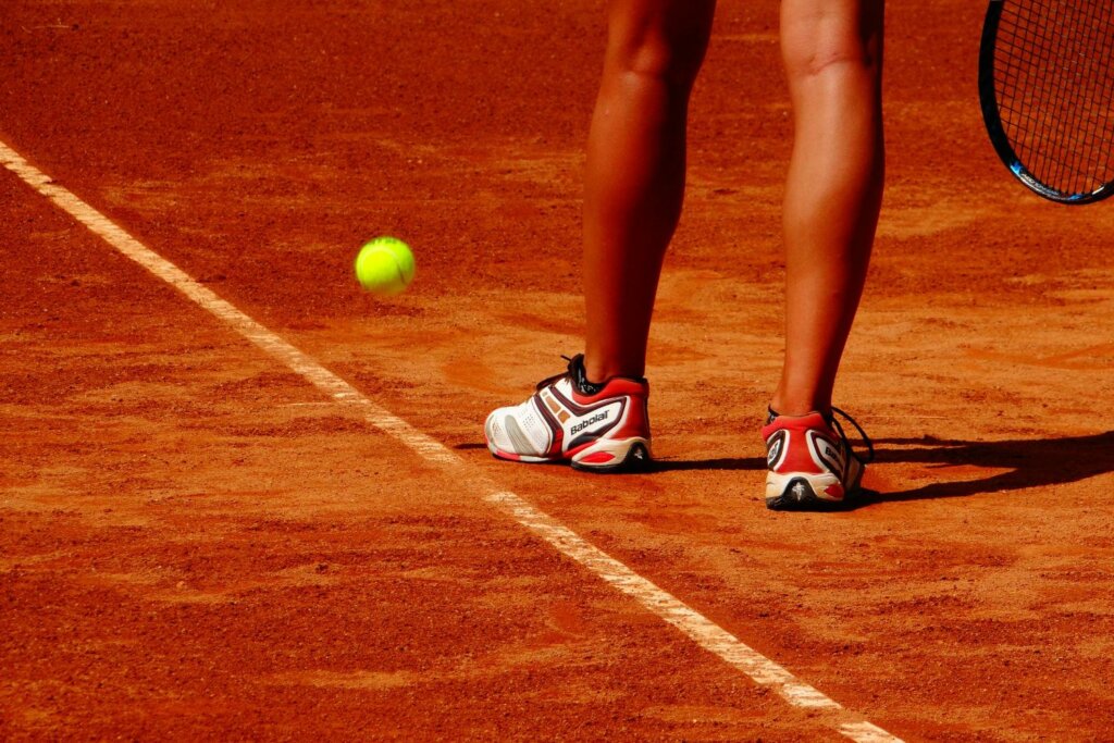 court en sable, chaussure de tennis noir, rouge et blanc, raquette et balle